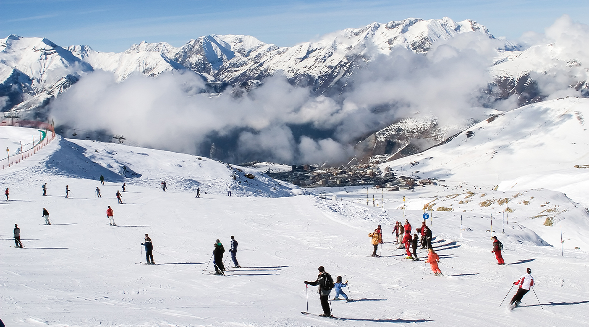A huge impressive mountain range with snowy hills and people skiing on the slopes